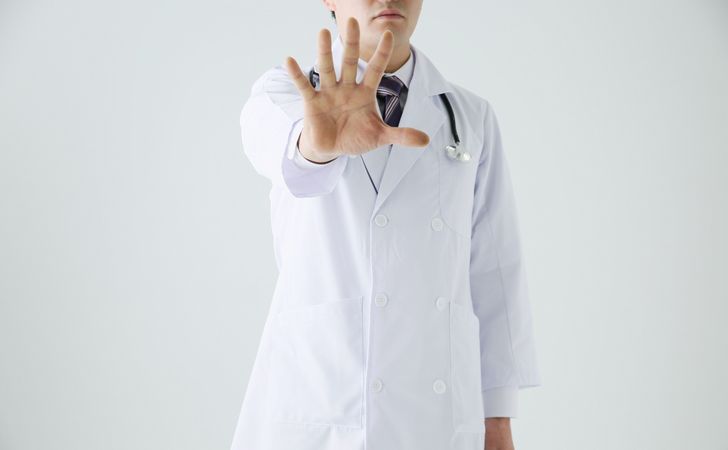 お医者さんが手のひらを前に突き出し立っている